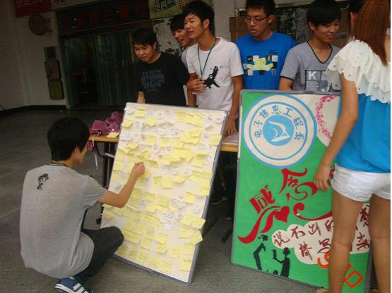 图为：同学们正将对老师的祝福贴在KT板上